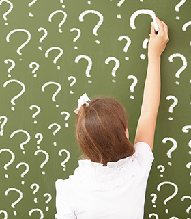 girl writing question marks on chalkboard